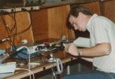 Color photograph of an individual sitting at a desk and examining equipment.