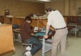 Color photograph of two individuals huddled at a desk, examining equipment.