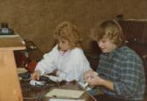 Color photograph of two individuals sitting at a desk, examining equipment.