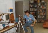 Color photograph of an individual sitting on a stool and examining equipment.
